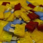 Fusibles automotrices apilados de varios colores sobre fondo amarillo, autopartes eléctricas en Ecatepec