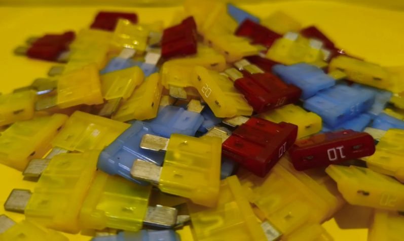 Fusibles automotrices apilados de varios colores sobre fondo amarillo, autopartes eléctricas en Ecatepec